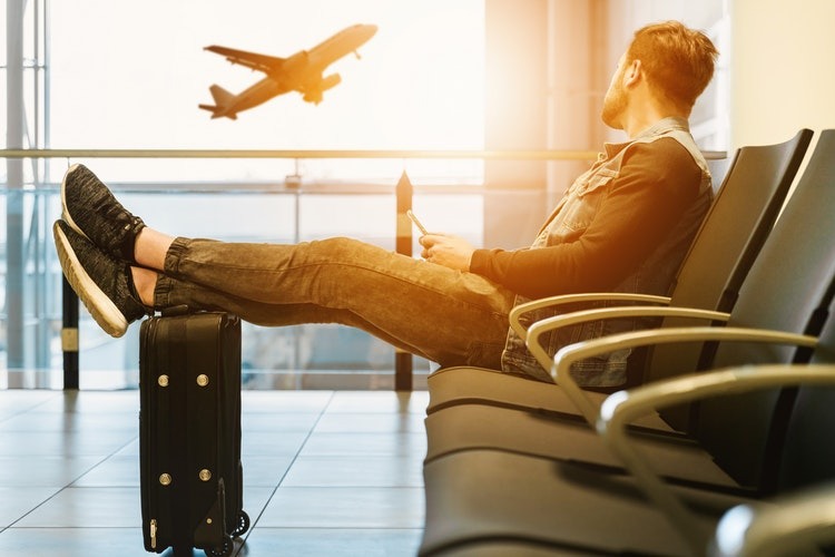 man sitting on a chair with feet on luggage while looking at an airplane