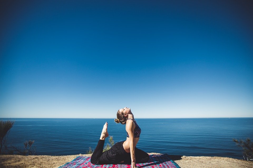 A woman, alone, doing a yoga pose beside the ocean