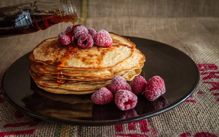 pile of pancakes, raspberries on top of pancakes, maple syrup being poured