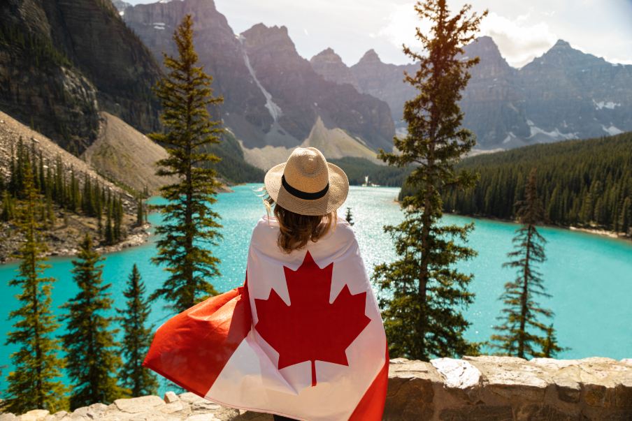 A woman draped in a Canadian flag against a mountainous background.