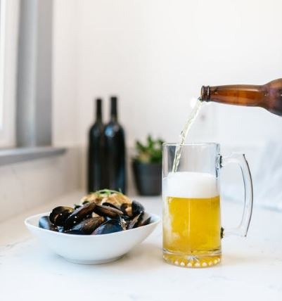 a-bowl-of-seafood-beer-being-poured-into-the-mug-two-bottles-a-plant